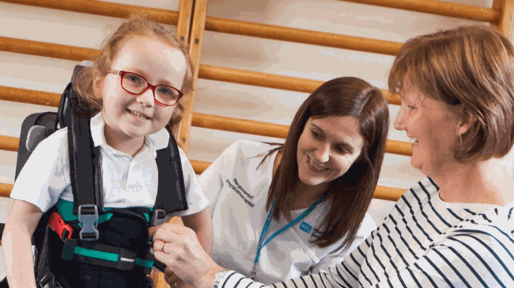 A young child in a paediatric walking aid with their parent.